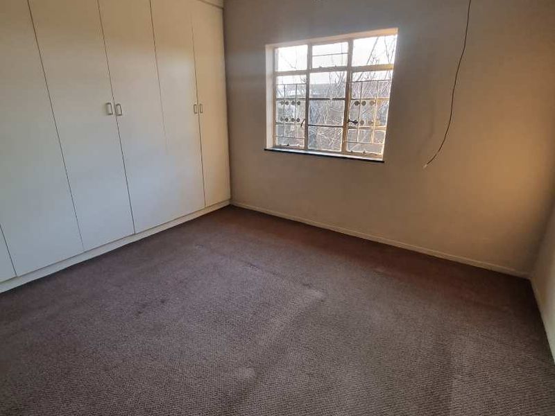 An empty bedroom featuring built-in cupboards, carpeted flooring, and a steel-framed window, requiring minor cosmetic updates and electrical repair.