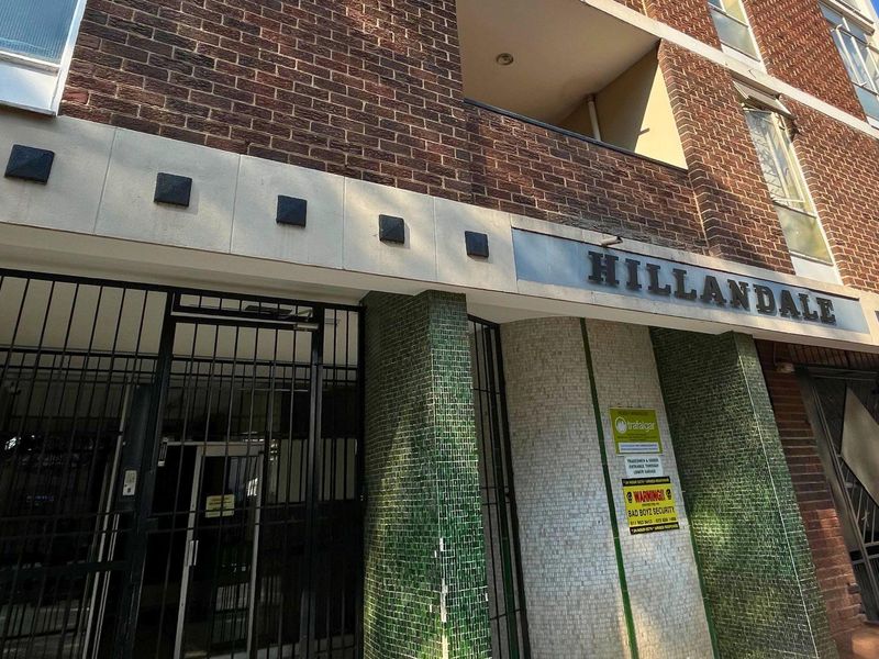 Front entrance view of the Hillandale apartment building, featuring a brick facade, security gate, and decorative mosaic tile detailing.