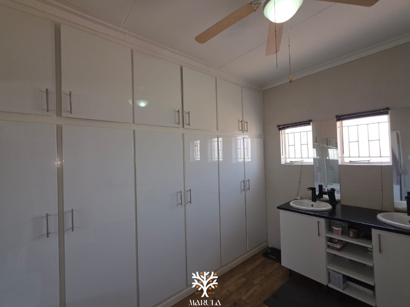 A bathroom featuring extensive built-in white cabinetry, a double vanity with dark countertops, and a ceiling fan.