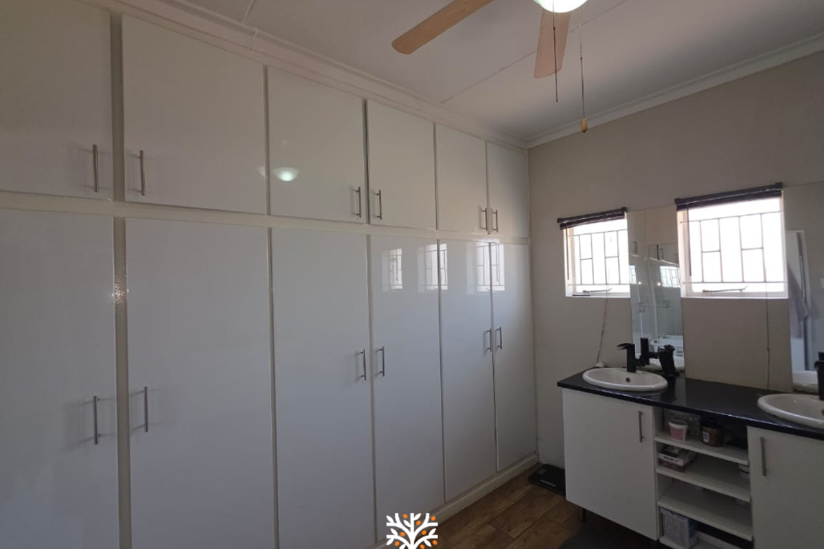 A bathroom featuring extensive built-in white cabinetry, a double vanity with dark countertops, and a ceiling fan.