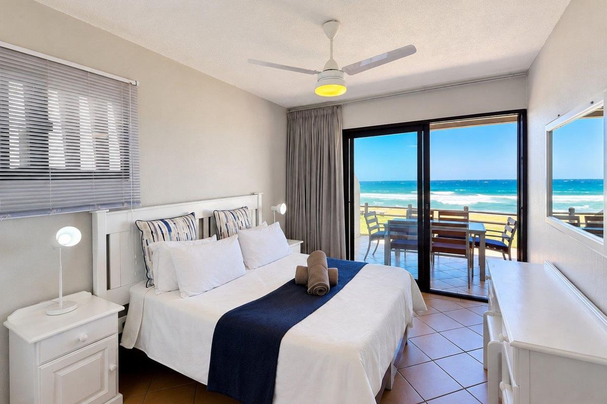 A well-maintained bedroom featuring tiled flooring, a ceiling fan, and sliding glass doors that open onto a balcony with ocean views.