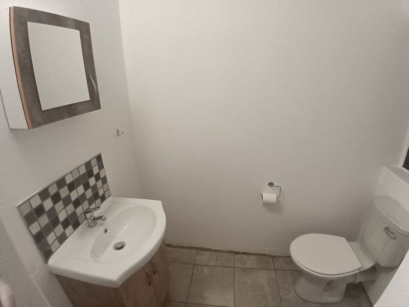 A compact bathroom featuring a vanity cabinet with basin, tiled splashback, and a standard toilet, with neutral wall finishes and tiled flooring.