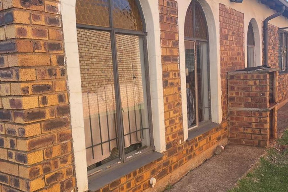 Rear exterior view of a face brick house featuring arched windows, a built-in brick braai, and a concrete walkway.