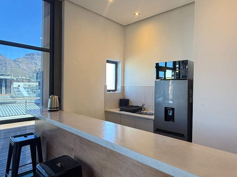 A modern kitchen area featuring a stone breakfast bar, recessed lighting, and a tiled backsplash, with large windows offering scenic mountain views.