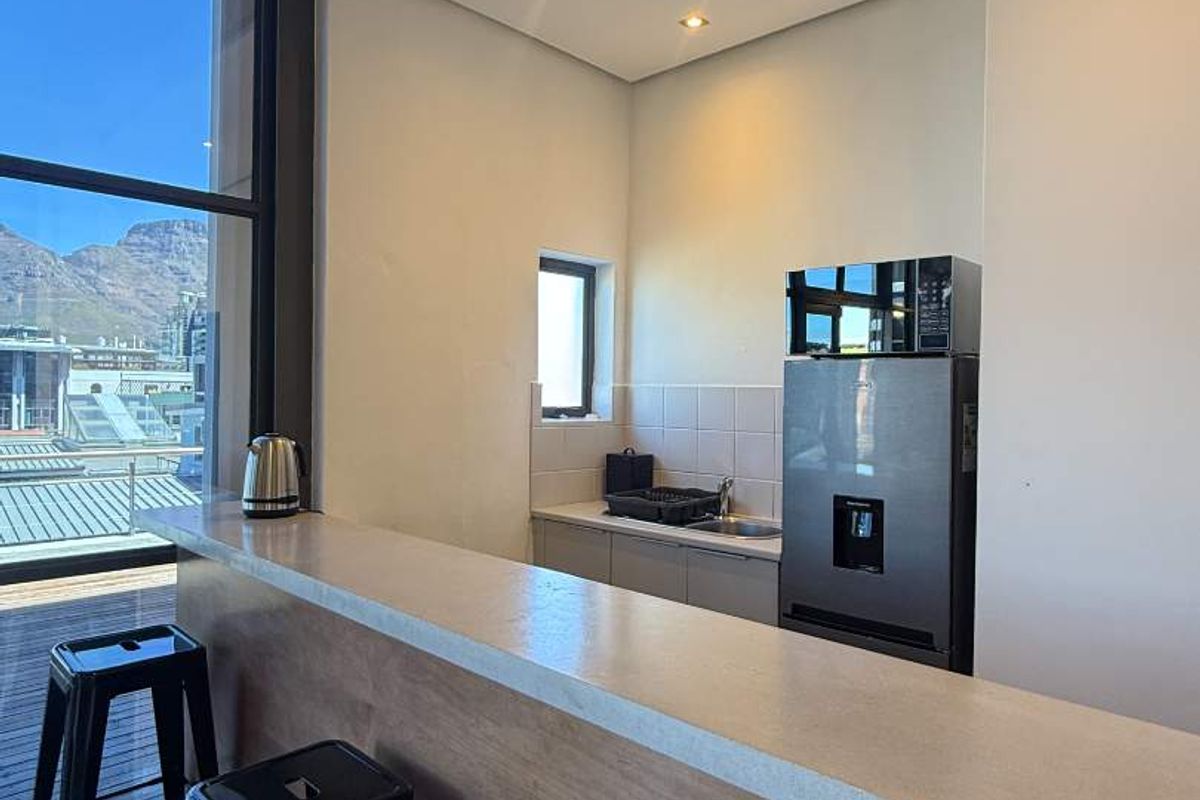 A modern kitchen area featuring a stone breakfast bar, recessed lighting, and a tiled backsplash, with large windows offering scenic mountain views.
