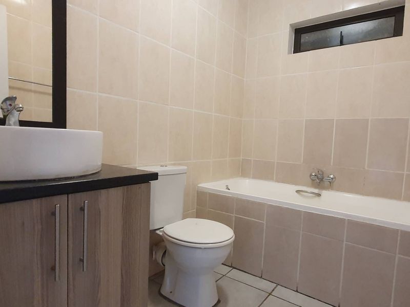 A functional bathroom featuring a vanity with a vessel sink, a standard toilet, and a tiled bathtub area with neutral wall finishes.