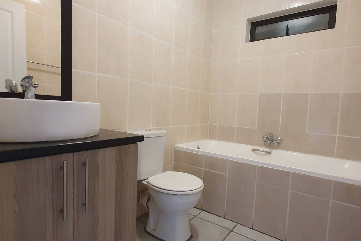 A functional bathroom featuring a vanity with a vessel sink, a standard toilet, and a tiled bathtub area with neutral wall finishes.