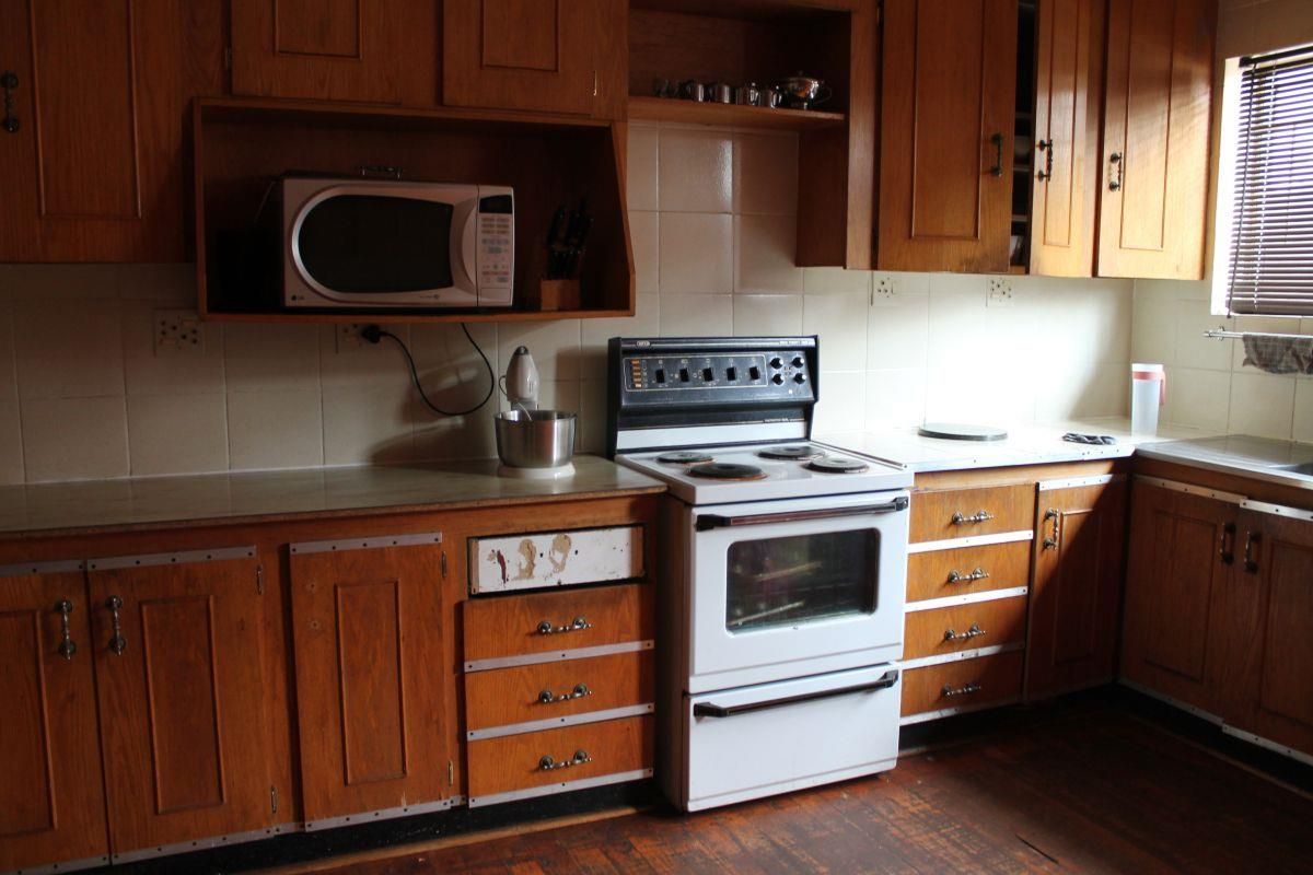 A dated kitchen featuring wooden cabinetry, tiled backsplash, and a freestanding stove, offering significant potential for modernization and renovation.