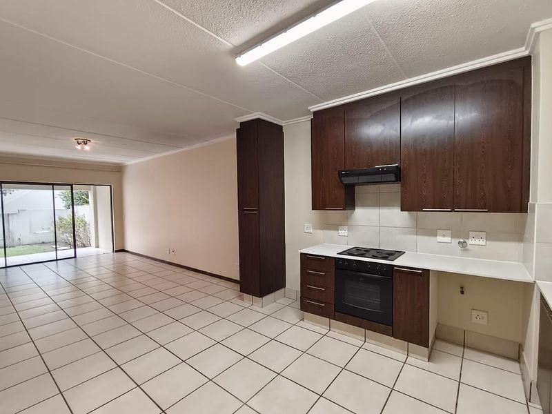 Spacious open-plan living and kitchen area featuring dark wood cabinetry, built-in oven and hob, tiled flooring, and sliding door access to the exterior.