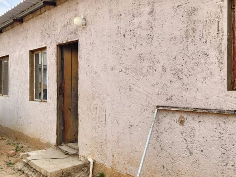 Rear exterior view of the property featuring textured plaster walls, steel-framed windows with security bars, and a corrugated metal roof overhang.