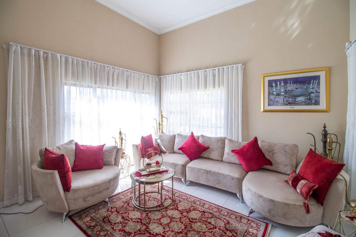 A bright and airy living room featuring large windows with elegant floor-to-ceiling curtains and neutral tiled flooring.