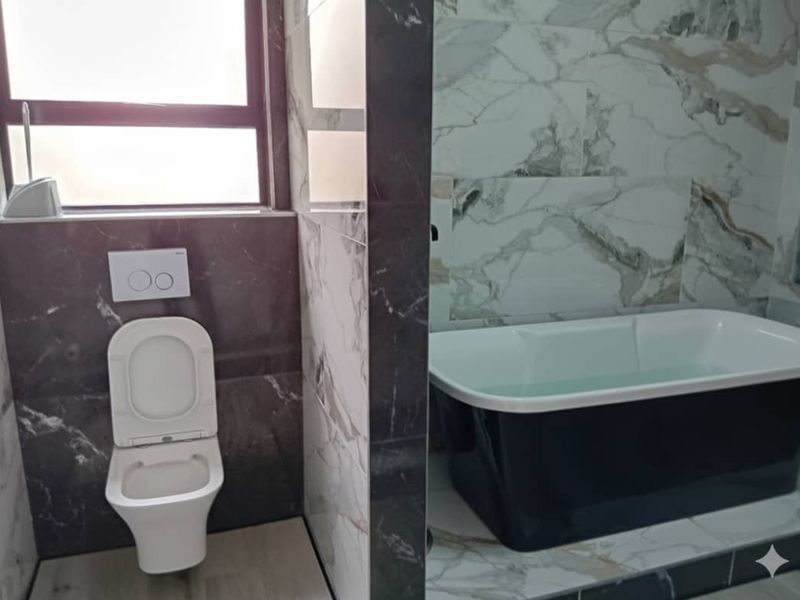 Modern bathroom featuring a wall-mounted toilet with concealed cistern and a sleek freestanding bathtub, complemented by elegant marble-effect wall tiling.