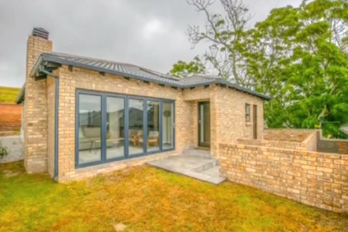 Rear view of a brick townhouse featuring large folding glass doors, a chimney, and a paved patio area leading to a garden.