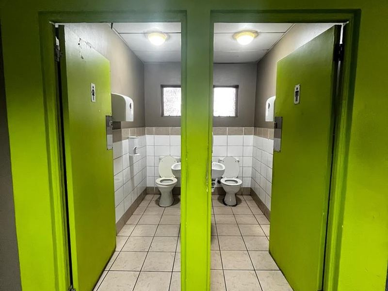 A commercial restroom facility featuring two separate stalls with tiled flooring, wall-mounted toilets, and basins.