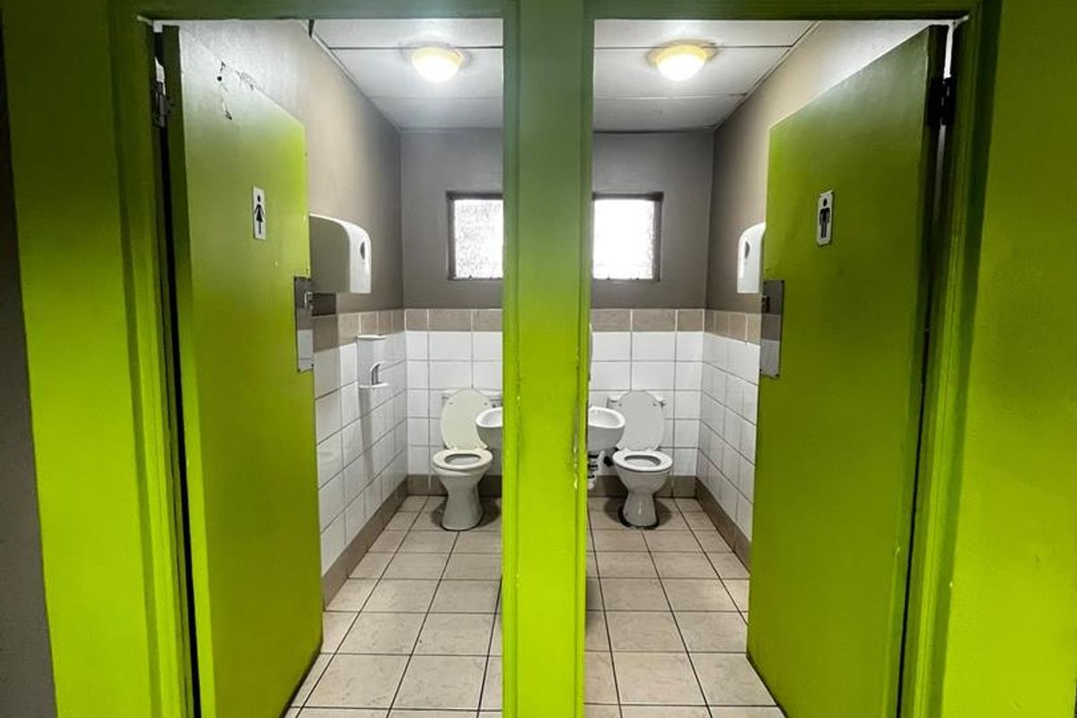 A commercial restroom facility featuring two separate stalls with tiled flooring, wall-mounted toilets, and basins.