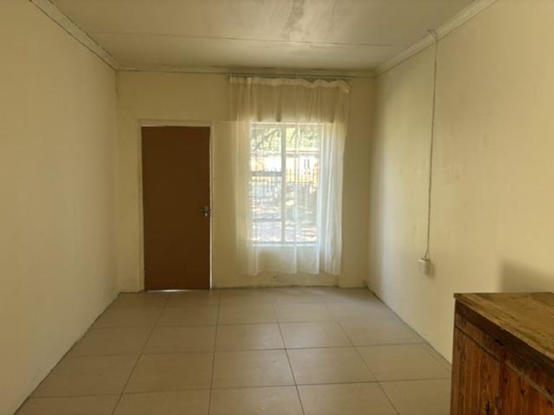 An empty living room featuring tiled flooring, a security door, and a window with a curtain rail, offering a blank canvas for interior design.