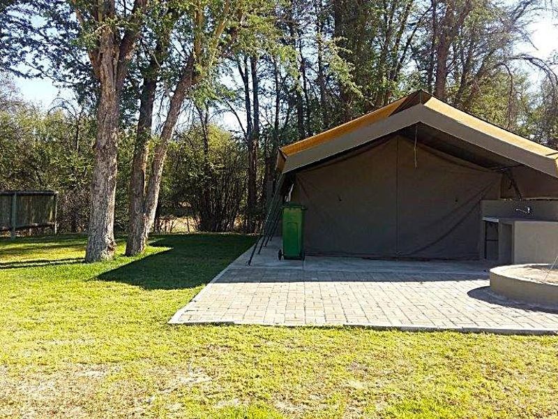 A safari-style tent accommodation featuring a paved patio, outdoor sink area, and a circular concrete fire pit set within a natural garden environment.