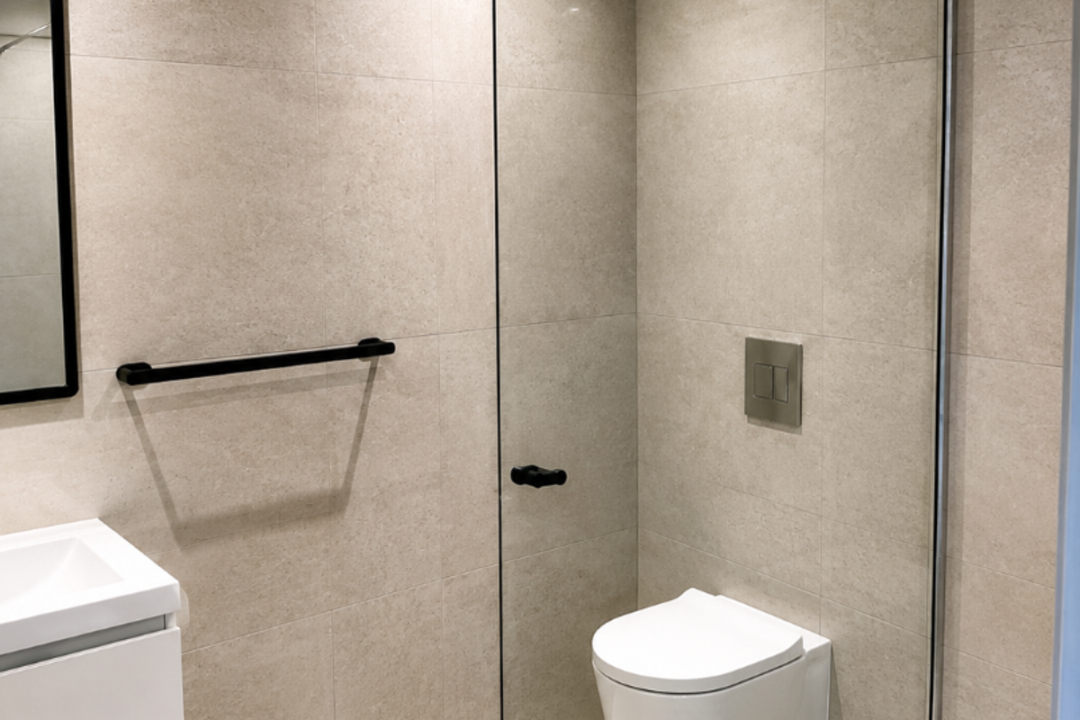 Modern bathroom featuring a wall-mounted toilet, glass shower screen, vanity basin, and neutral floor-to-ceiling tiling with contemporary black fixtures.
