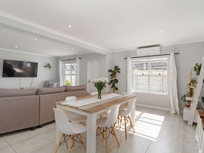 Bright open-plan living and dining area featuring neutral tiled flooring, recessed lighting, and a wall-mounted air conditioning unit.