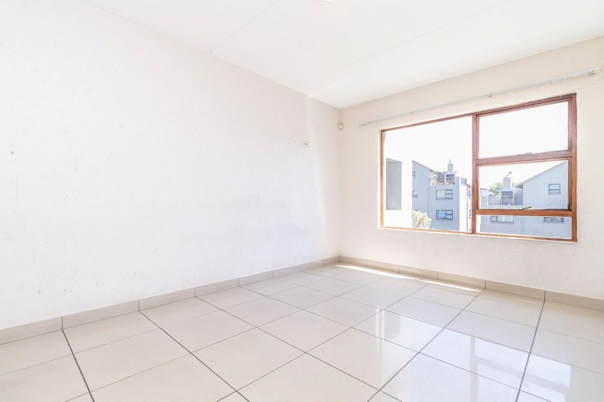 A bright, empty living area featuring neutral ceramic floor tiles and a large window with a wooden frame, offering a clean, blank canvas.