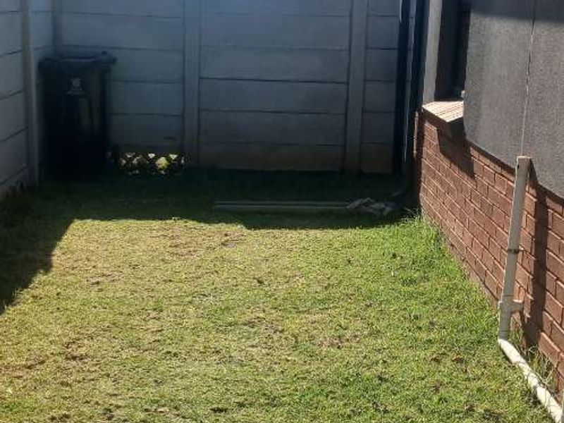A side or rear yard area featuring a lawn, enclosed by a precast concrete boundary wall and adjacent to the brick exterior of the house.