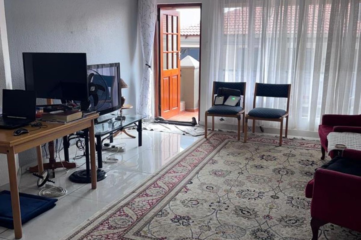 A bright living room featuring large windows with sheer curtains, tiled flooring, and direct access to an outdoor patio area.