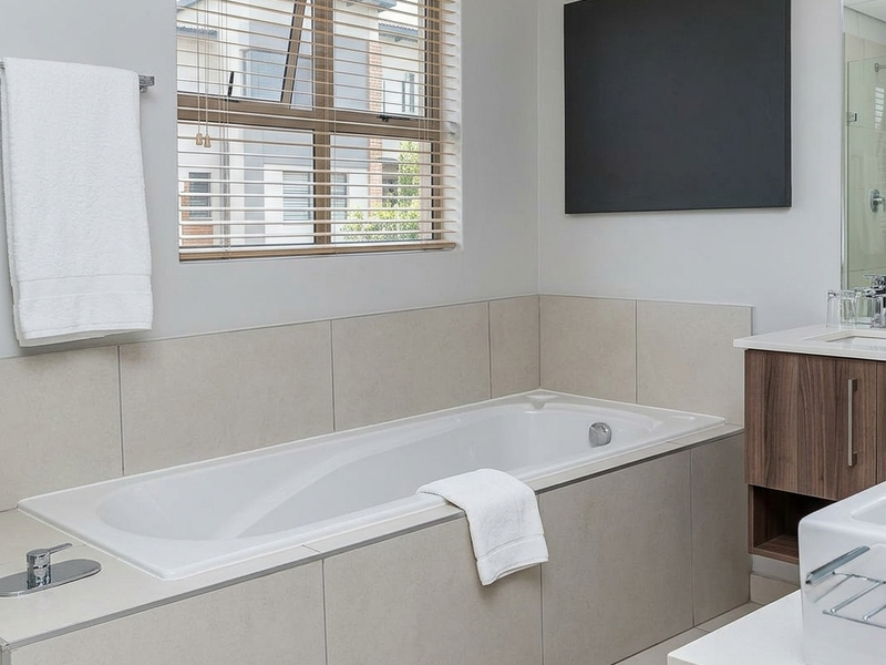 Modern bathroom featuring a built-in bathtub, tiled surround, vanity cabinet with integrated basin, and neutral finishes.