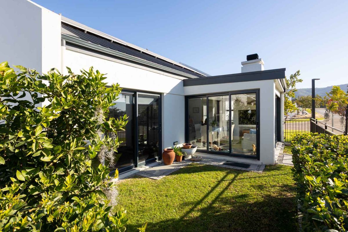 Rear view of the property featuring a well-maintained lawn, modern sliding glass doors, and solar panels installed on the roof.
