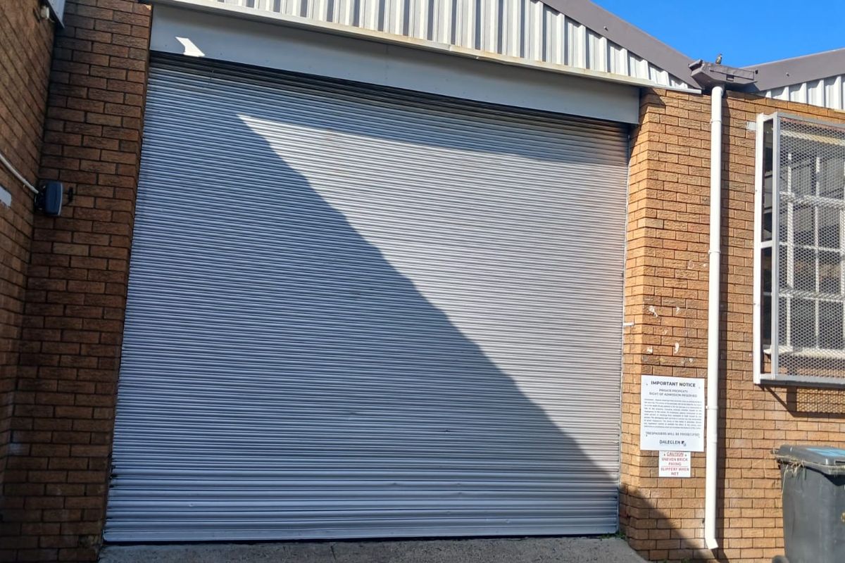 Industrial exterior view featuring a large metal roller shutter door, face brick walls, and security window grilles.