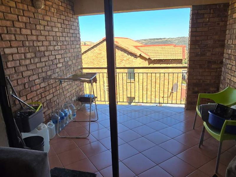 Covered balcony featuring exposed brick walls, tiled flooring, and a metal balustrade, offering an outdoor space accessible via a sliding glass door.