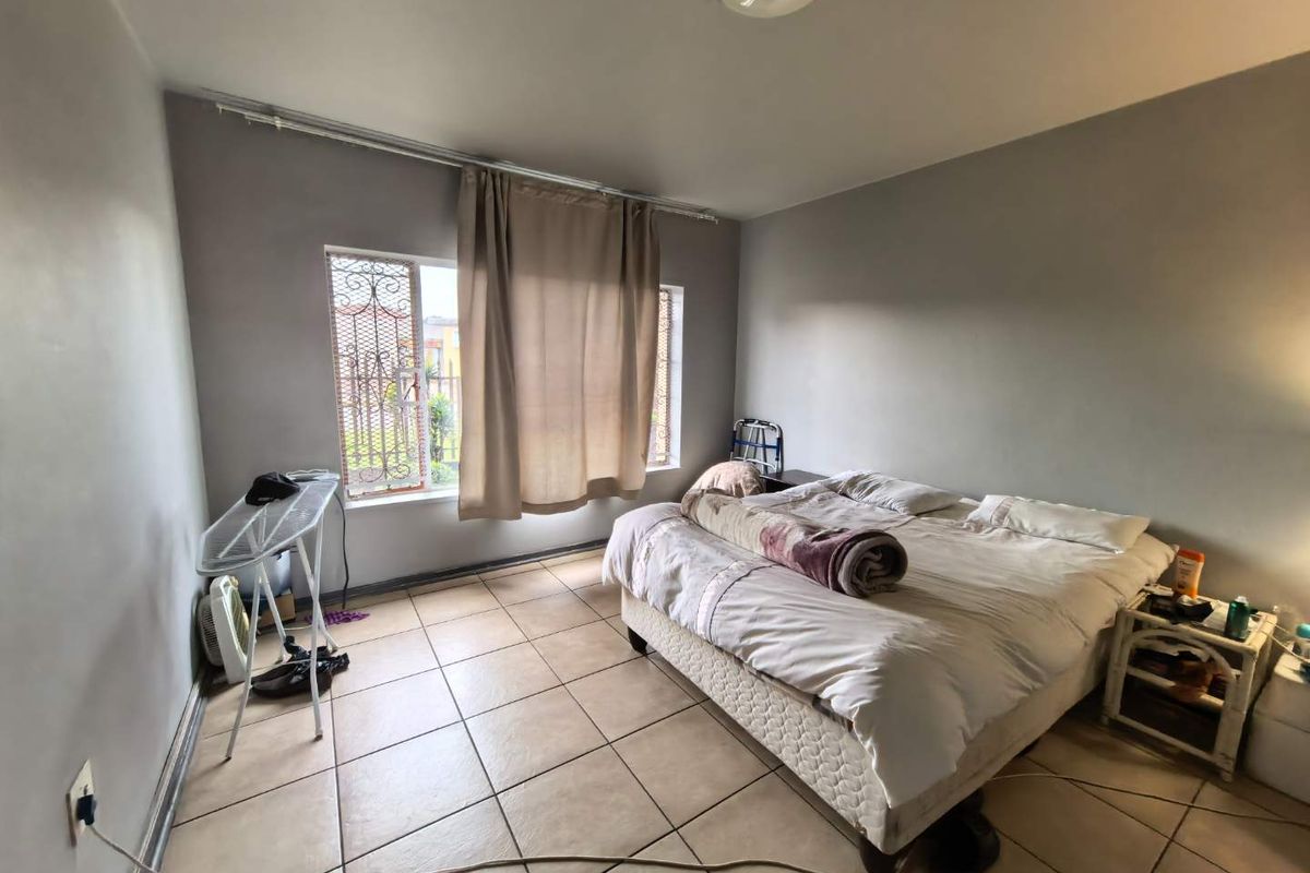 A bedroom featuring tiled flooring, neutral wall paint, and a window with security bars, providing a functional living space.