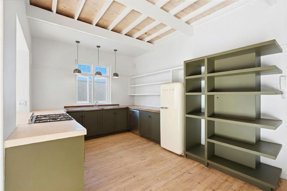 A bright kitchen featuring olive green cabinetry, timber countertops, exposed beam ceiling, and integrated shelving, creating a warm and functional culinary space.