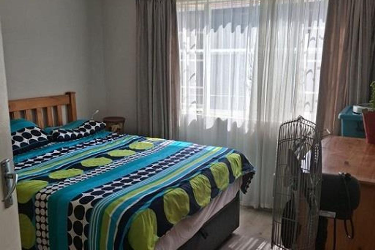 A functional bedroom featuring wood-look flooring, a large window with curtains, and a ceiling-mounted light fixture.