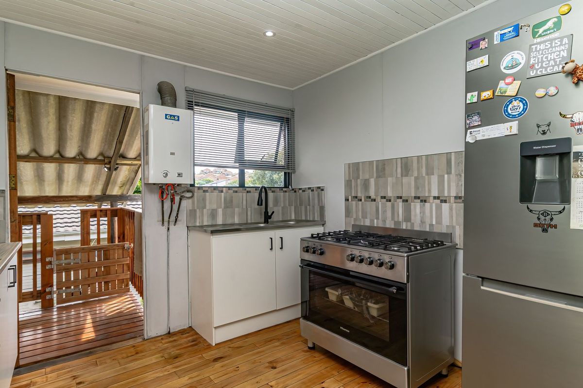A functional kitchen featuring a gas stove, oven, sink, and tiled splashback, with direct access to an outdoor wooden deck area.