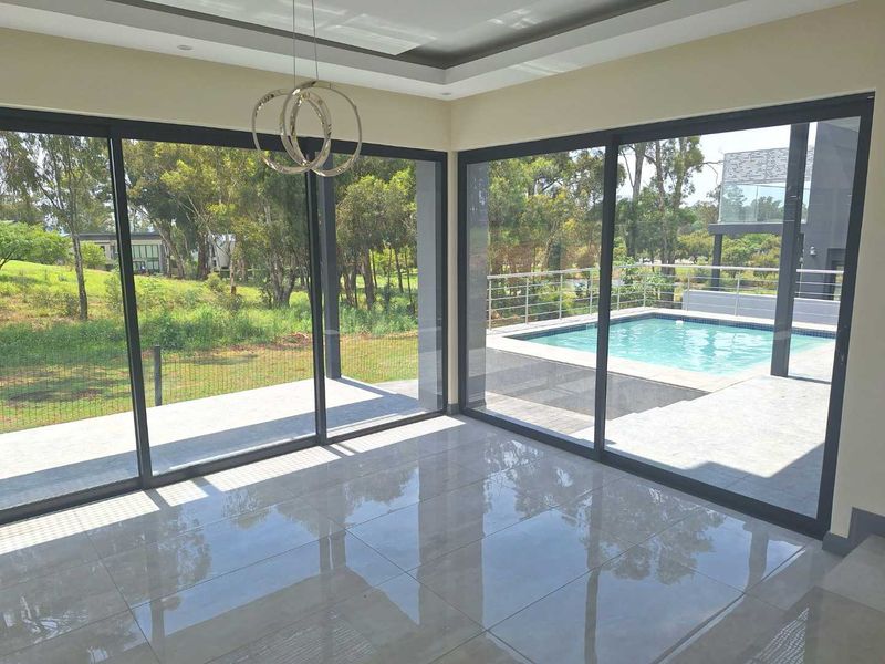 Bright, modern living area featuring large format floor tiles, recessed ceiling lighting, and expansive sliding doors opening onto a private pool deck.