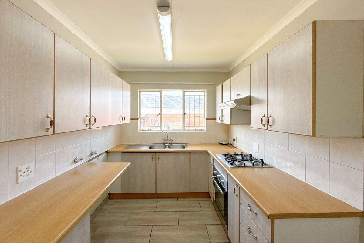 A functional galley-style kitchen featuring light-toned cabinetry, laminate countertops, a built-in gas hob, oven, and a double-basin sink with tiled splashbacks.