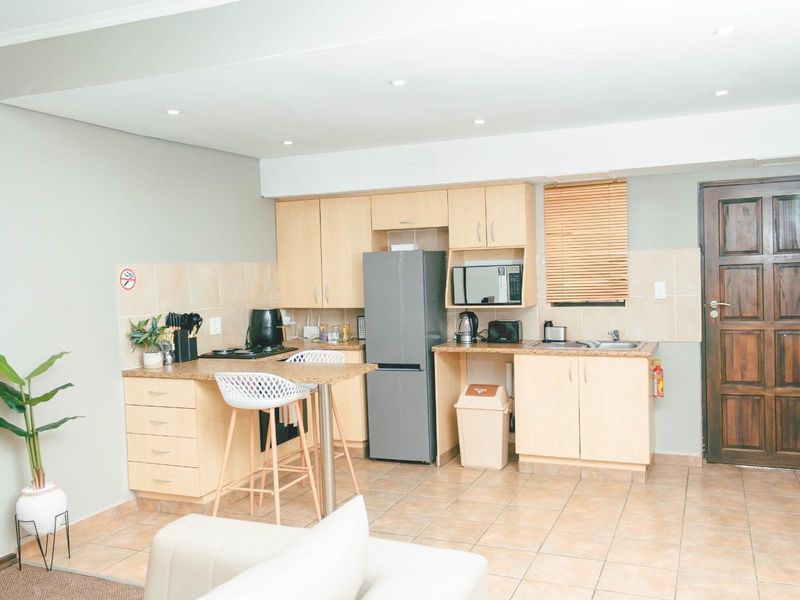 Open-plan kitchen featuring light wood cabinetry, laminate countertops, tiled backsplash, and integrated appliances, seamlessly connected to the living area.