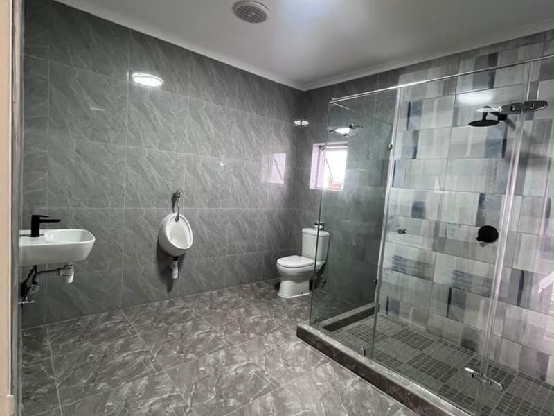 Modern bathroom featuring grey marble-look floor and wall tiles, a walk-in glass shower, wall-mounted basin, toilet, and a dedicated urinal.