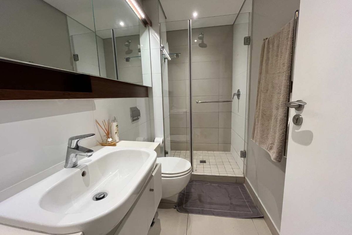 Modern bathroom featuring a glass-enclosed shower, wall-mounted toilet, and a vanity with an integrated basin and mirrored cabinetry.