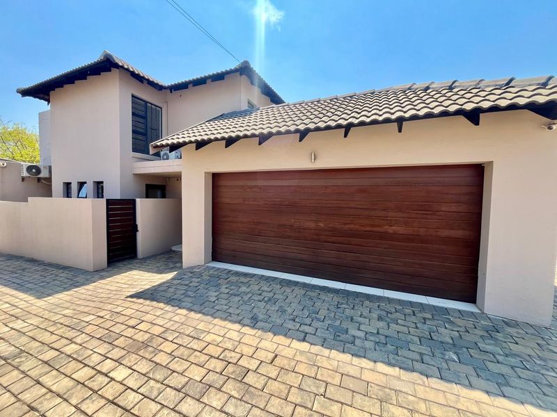 Front elevation of the townhouse featuring a paved driveway, a wooden garage door, and a secure entrance gate.