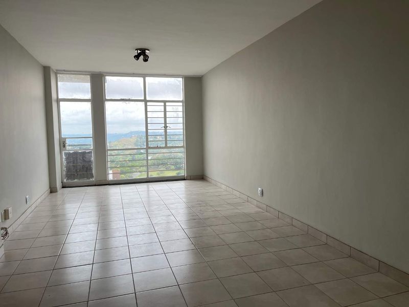 A bright, empty living room featuring neutral tiled flooring, large windows with scenic views, and access to an outdoor area.