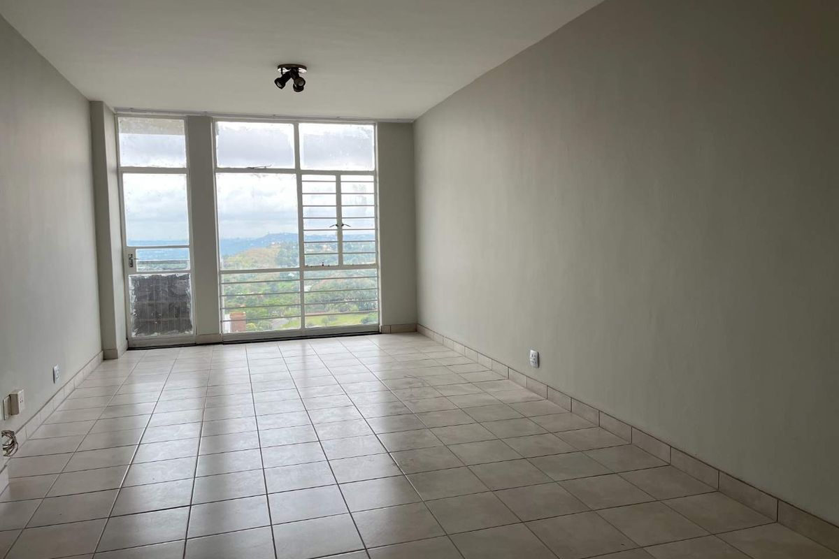 A bright, empty living room featuring neutral tiled flooring, large windows with scenic views, and access to an outdoor area.