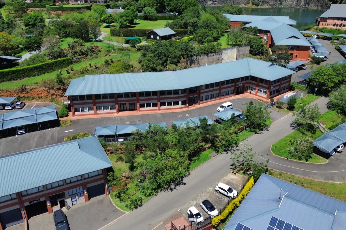 Aerial view of a professional office complex featuring brick buildings with metal roofing, extensive landscaped grounds, and multiple covered parking bays.