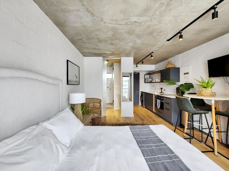 Modern open-plan studio apartment featuring an exposed concrete ceiling, painted brick walls, sleek kitchen cabinetry, and high-quality laminate flooring throughout.