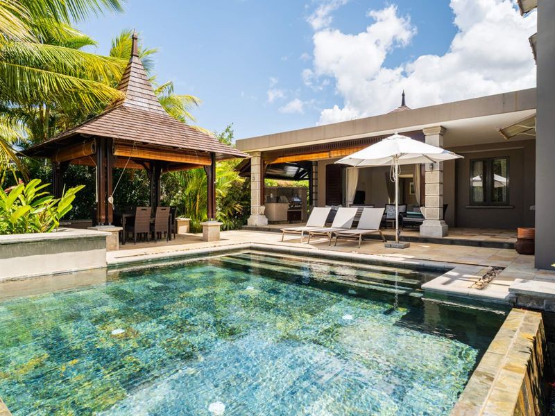 A well-maintained outdoor pool area featuring a stone-tiled deck, a covered patio space, and a traditional gazebo structure.