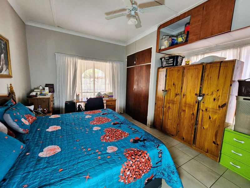 A bedroom featuring tiled flooring, a ceiling fan, and built-in wooden cupboards with overhead storage units.