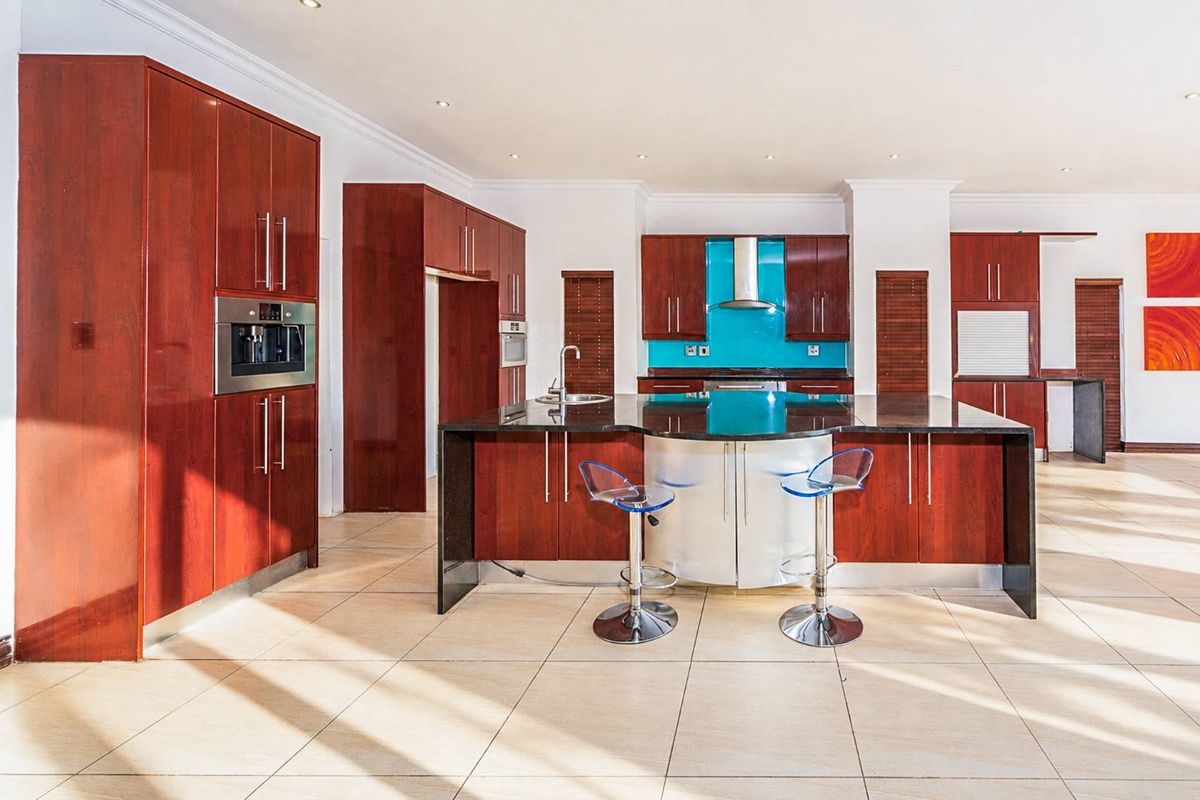 Spacious kitchen featuring dark wood cabinetry, a large central island with breakfast bar, integrated appliances, and a vibrant blue glass splashback.