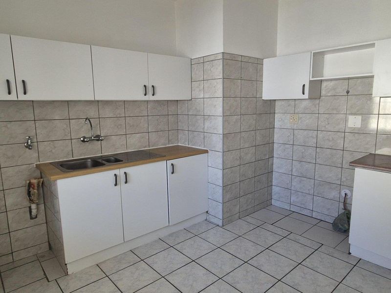 A functional kitchen featuring white built-in cabinetry, laminate countertops, tiled splashbacks, and tiled flooring, offering a clean and practical workspace.