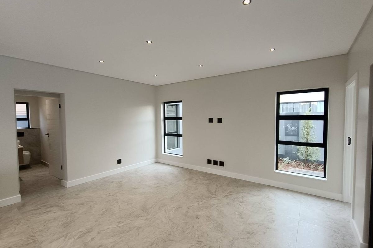 A bright, modern bedroom featuring neutral tiled flooring, recessed downlighting, and large black-framed windows with views of the garden.