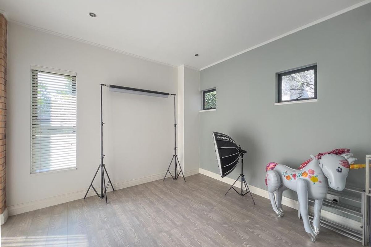 A bright, neutral-toned bedroom featuring modern laminate flooring, recessed ceiling lighting, and dual-aspect windows with fitted blinds.